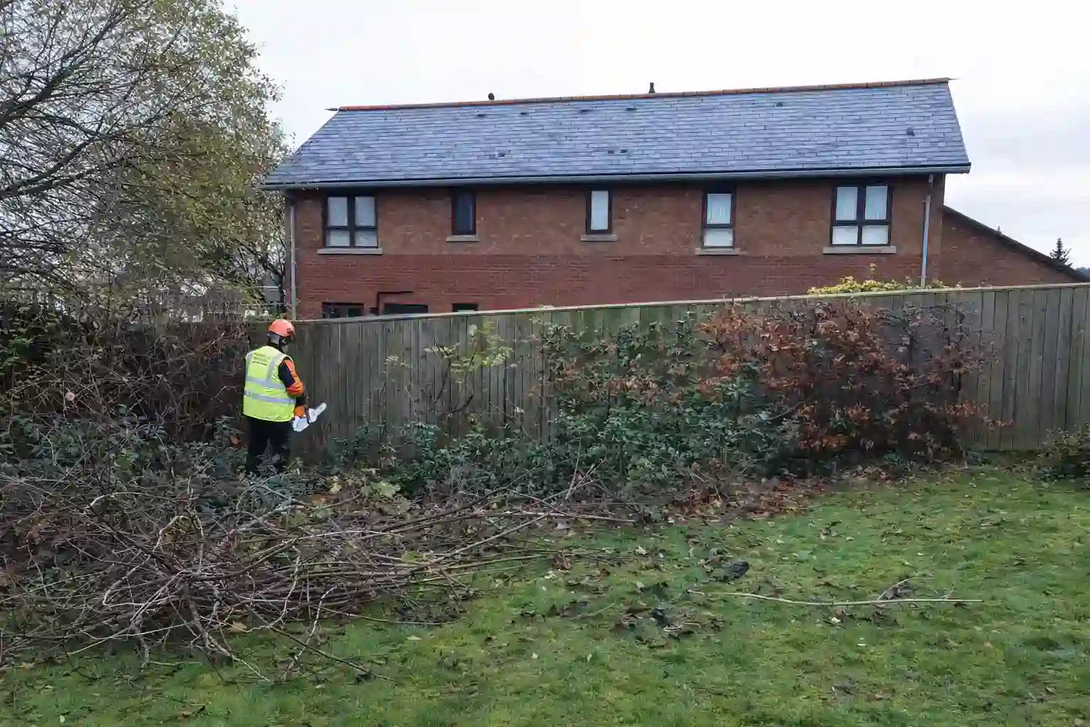 Grounds maintenance worker using battery-powered equipment beside a garden fence